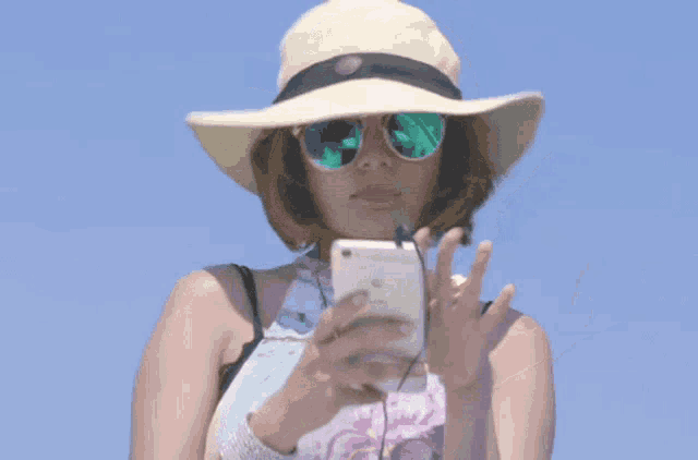 a woman wearing a hat and sunglasses holds a white iphone
