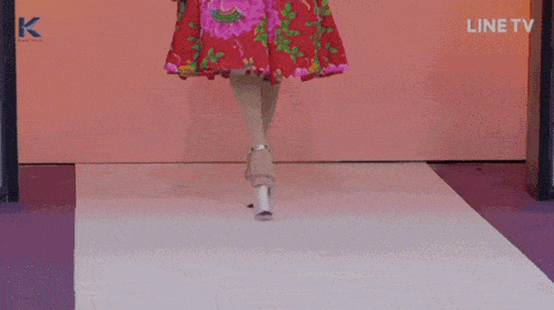 a woman in a red dress walks down a runway with a line tv logo in the background