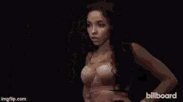 a naked woman is standing in front of a black wall with her arms behind her head .