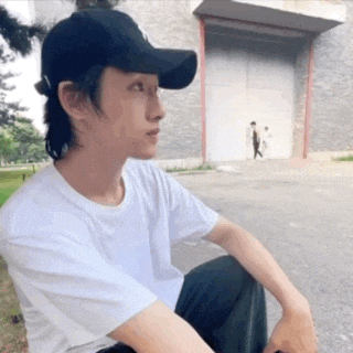 a man wearing a black hat and a white shirt is sitting in front of a building .