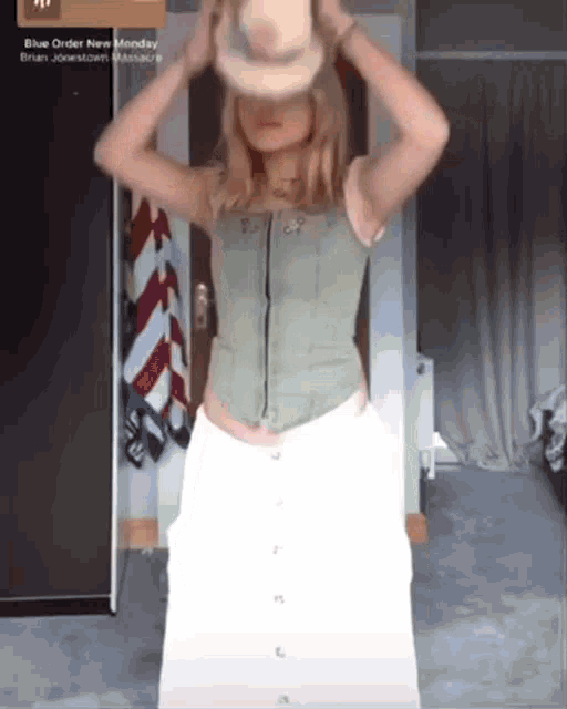 a woman wearing a green top and white pants is holding a cowboy hat in front of her face