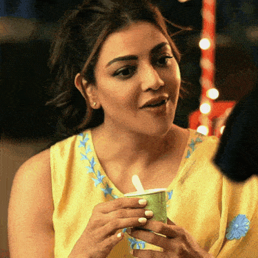 a woman in a yellow top is holding a green cup with a white spoon in it