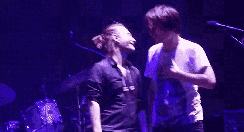 two men are kissing on a stage in front of a microphone in a dark room .