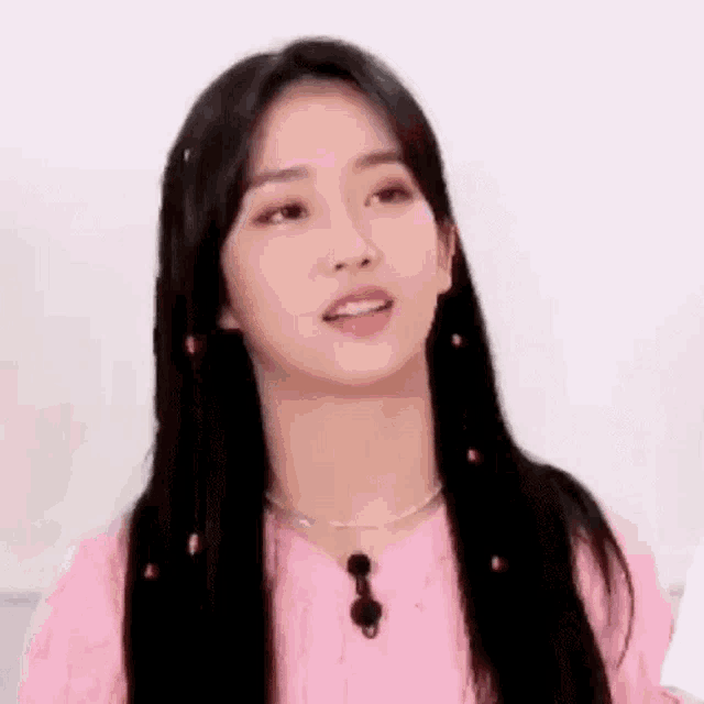 a close up of a woman wearing a pink sweater and a necklace .