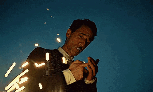 a man in a suit is smoking a cigarette in front of a blue sky .