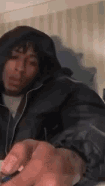 a man in a hooded jacket is sitting on a bed holding a lighter .