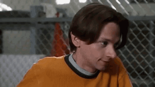 a young man wearing a yellow sweater and a black collar is standing in front of a chain link fence .