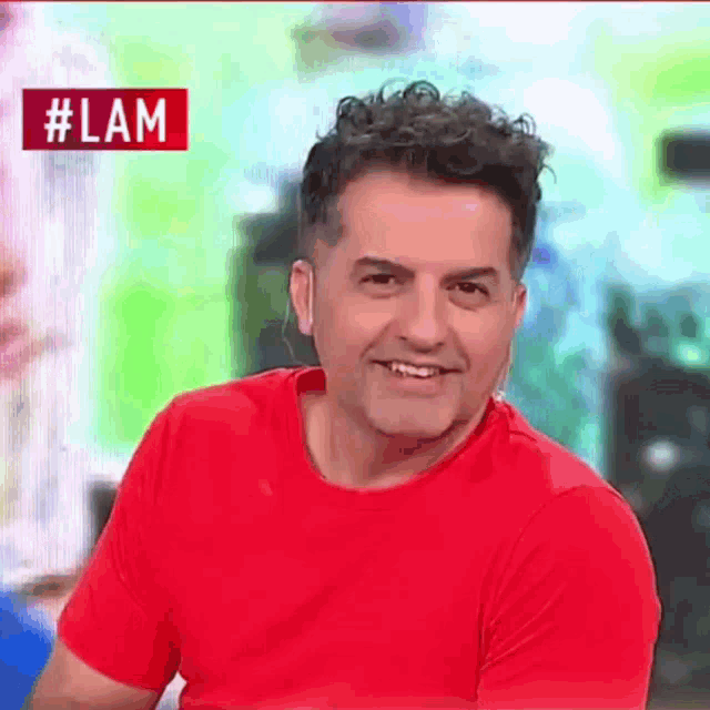 a man in a red shirt is smiling in front of a sign that says #lam on it .
