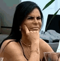 a woman is sitting at a table with her hand on her chin making a funny face .