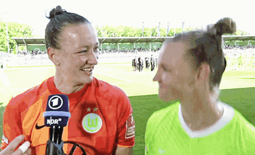 two female soccer players are talking to each other on a field with a microphone that says ndr on it
