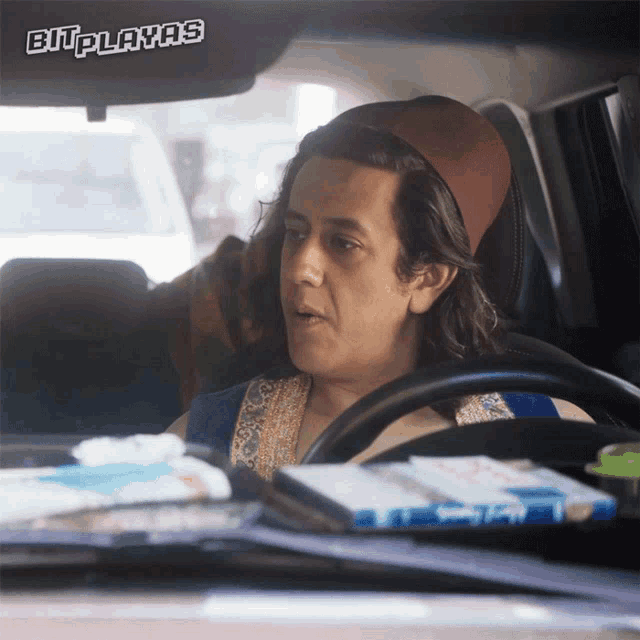 a man driving a car with a sticker on the windshield that says bit playas