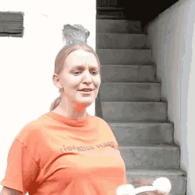 a woman in an orange t-shirt is standing in front of stairs .