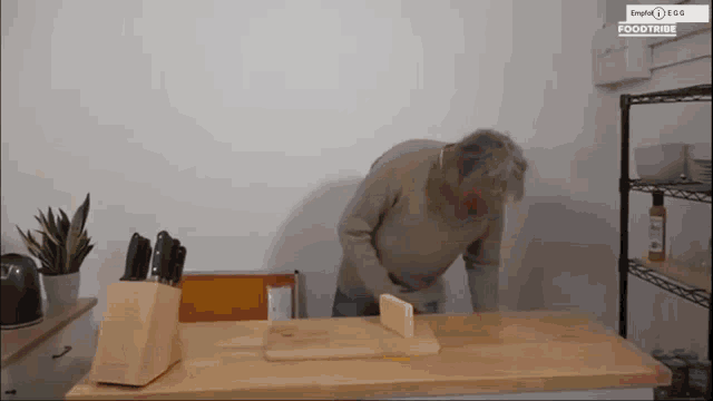 a man is cutting a piece of cheese on a cutting board with a knife block in the background