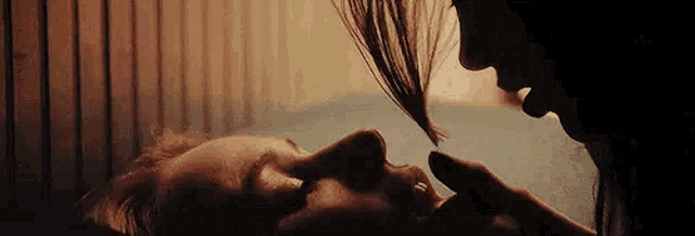 a woman is touching a man 's face while they are laying on a bed .