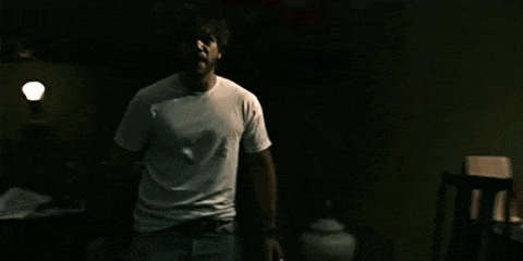 a man in a white shirt is standing in the dark in a room .