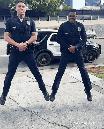 two police officers are jumping in front of a police vehicle