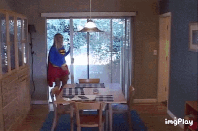 a woman in a superman costume is opening a sliding glass door in a living room .