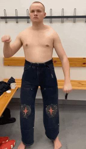 a man without a shirt is standing in a locker room with his fist up