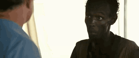 a man in a blue shirt is talking to a black man in a brown shirt .