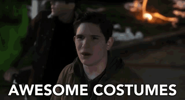 a young man is standing in front of a fire with the words `` awesome costumes '' written on the bottom .