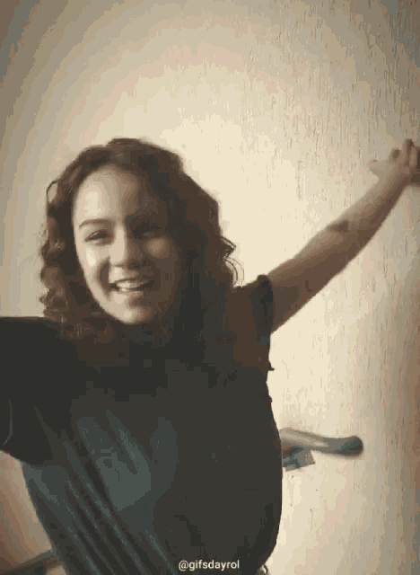 a girl is smiling with her arms outstretched in front of a wall with the gifsdayrol written on the bottom