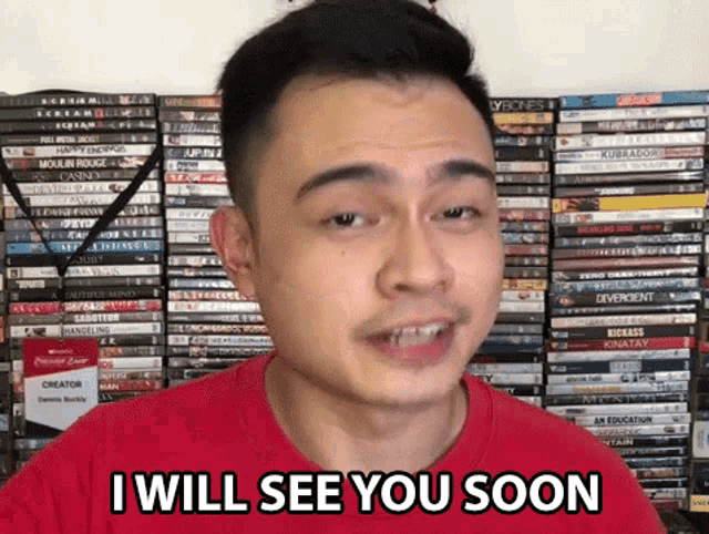 a man in a red shirt says i will see you soon in front of a stack of dvds