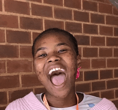 a girl with her tongue hanging out is standing in front of a brick wall