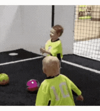 two young boys are playing soccer on a trampoline and one has the number 10 on his shirt .
