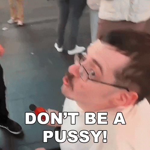 a man with glasses and a mustache is holding a microphone and saying " don 't be a pussy "