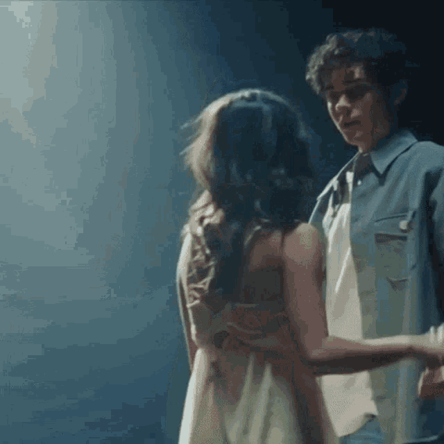 a man and a woman are dancing together in a dark room . the woman is wearing a white dress .