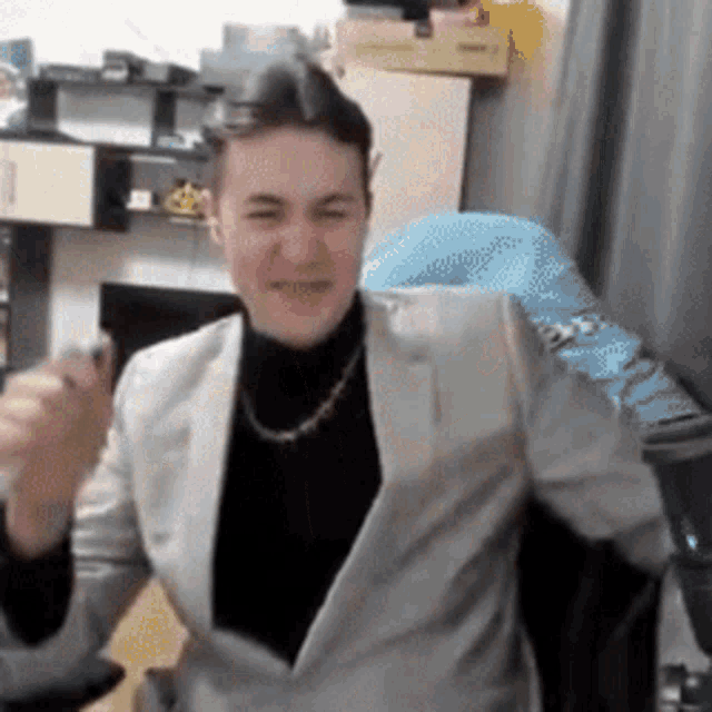 a man in a suit and turtleneck is sitting in a chair in a room .