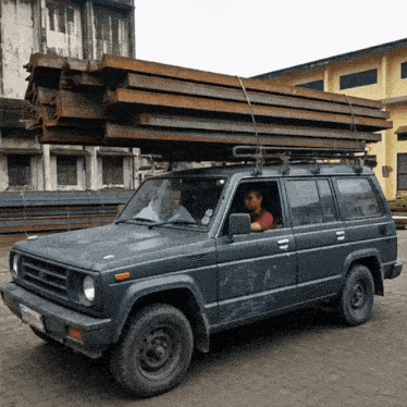 a man is sitting in the driver 's seat of a car with a stack of metal on the roof