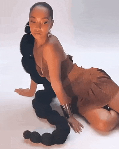 a woman in a brown dress is kneeling down on the floor with her hair in a braid .