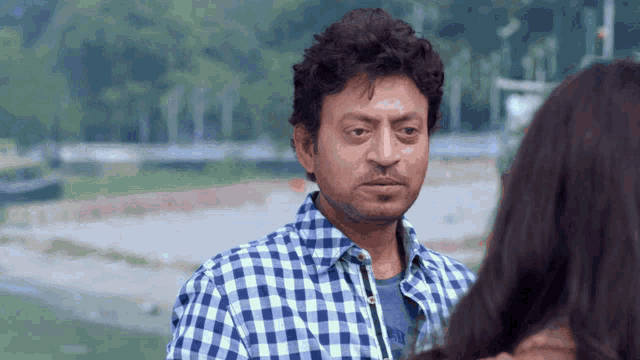 a man in a blue and white plaid shirt is looking at a woman