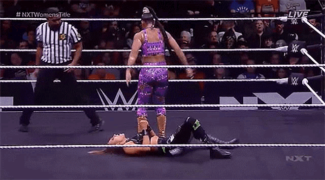two women are wrestling in a wrestling ring while a referee stands behind them .