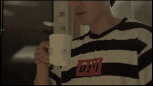 a man wearing a striped shirt with a red 0 on it drinks from a mug