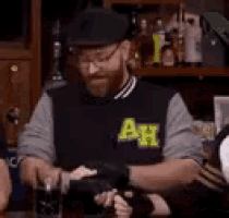 a man with a beard wearing a black jacket with the letter a on it is sitting at a table .