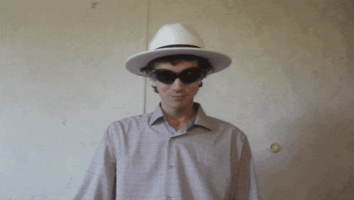 a man wearing a hat and sunglasses covering his mouth with his hand