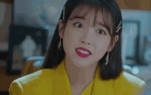 a woman wearing a yellow jacket and earrings is making a funny face .