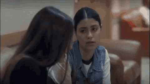 two young women are sitting next to each other on a couch and talking to each other .