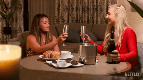 two women are sitting at a table with a bottle of champagne and a tray of food