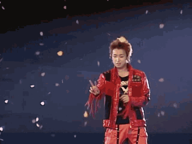 a man in a red jacket and red pants is standing on a stage with petals falling around him