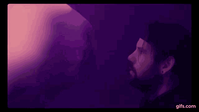 a man with a beard is standing in front of a pink and purple light .