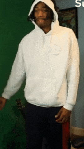 a man wearing a white hoodie is standing in front of a green wall
