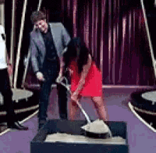 a woman in a red dress is shoveling sand into a box on a stage