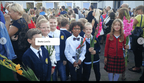 a group of children are holding flowers in front of a crowd and the name beata lovelis is visible
