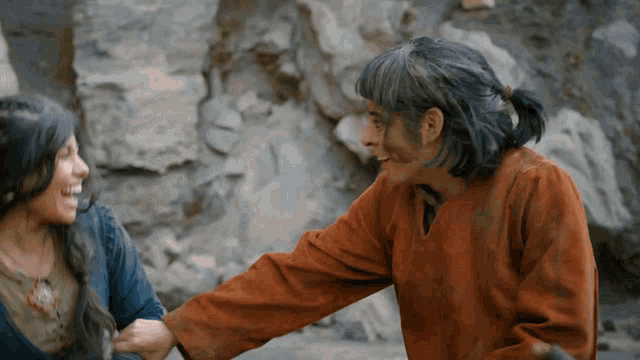 a man and a woman are holding hands in front of a rock wall