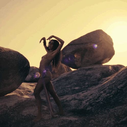 a woman in a bikini is standing on a rocky hillside
