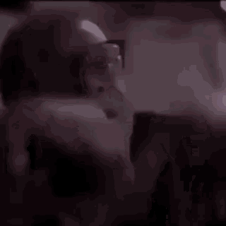a man with glasses and a beard is looking at something in the dark .
