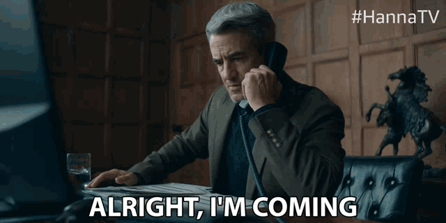 a man talking on a phone with the words alright i 'm coming